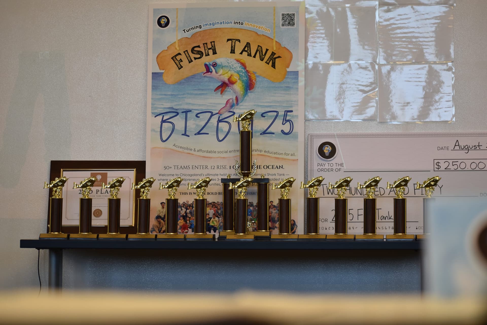 Fish Tank 2025 trophies lined up in front of the event poster