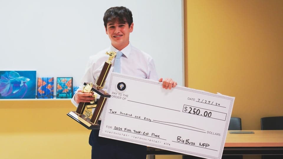 A Fish Tank winner holding a trophy and a $250 prize check